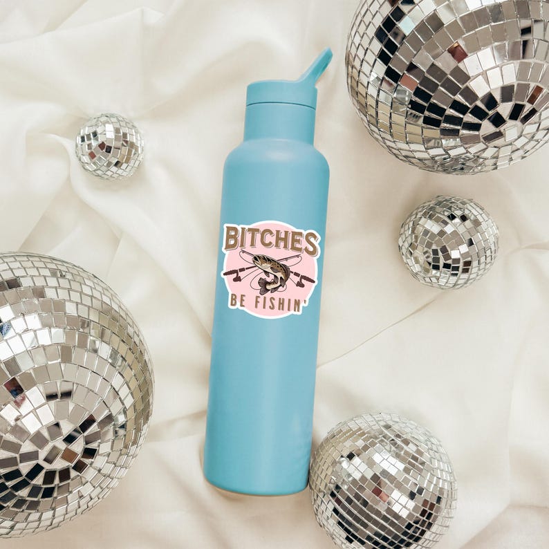 May include: A light blue water bottle with a pink and brown sticker that says "Bitches Be Fishin'" and features a cartoon fish with fishing rods. The sticker is on a light blue water bottle.