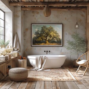 May include: A white freestanding bath with a beige towel draped over the edge, set in a rustic bathroom with wood beams, a large framed painting of a tree, and a potted plant.