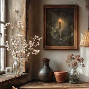 May include: A rustic wooden table with a framed print of a candle in a forest, a brown vase, a terracotta pot, and a glass vase with dried flowers.