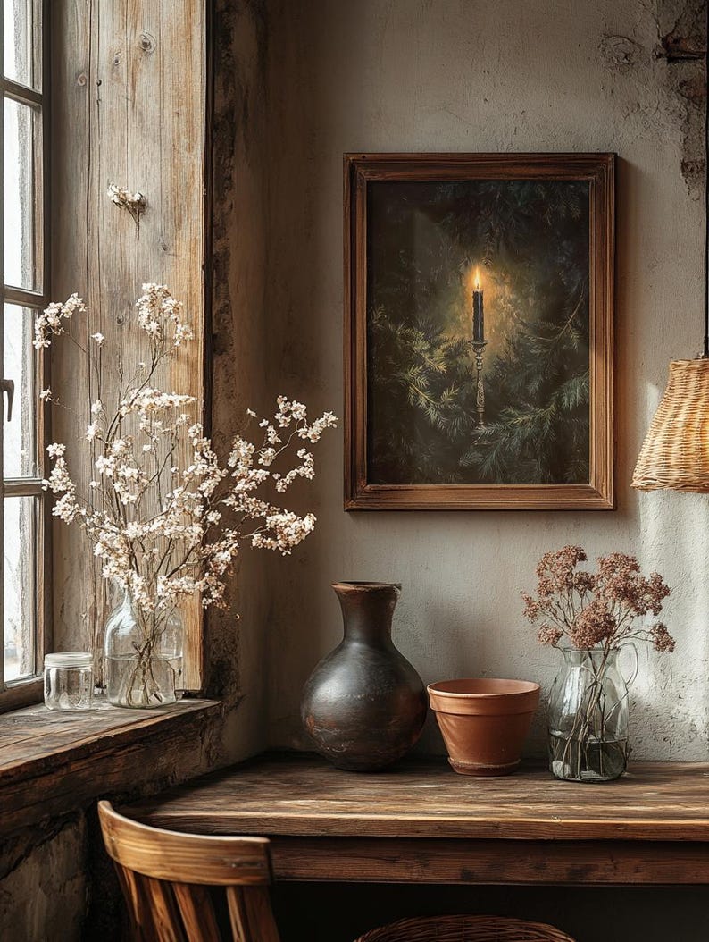 May include: A rustic wooden table with a framed print of a candle in a forest, a brown vase, a terracotta pot, and a glass vase with dried flowers.