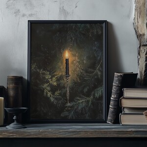 May include: A black framed print of a candle burning in a dark forest setting. The candle is on a silver candlestick and is surrounded by pine branches.