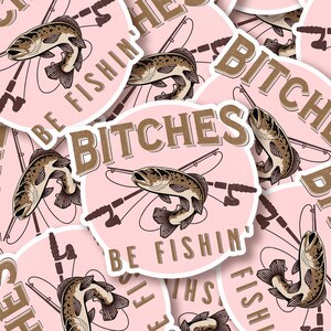 May include: Pink sticker with a brown fish and fishing rods, with the text "Bitches Be Fishin'" in brown lettering.