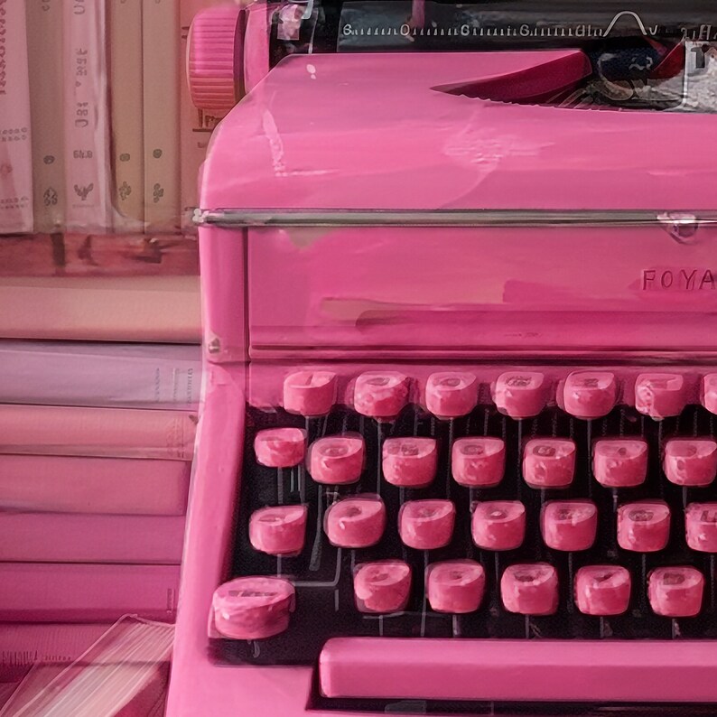 K&ouml;nnte beinhalten: Eine leuchtend pinkfarbene Vintage-Schreibmaschine mit einer schwarzen Tastatur und dem Wort "FOYA" auf der Seite.