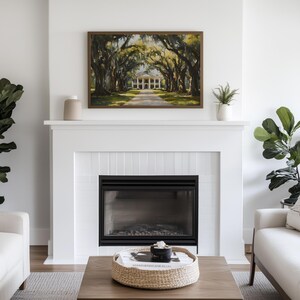 May include: A white fireplace with a black fireplace insert and a framed painting of a white mansion with a long driveway lined with trees. The painting is above the fireplace and there is a white vase on the mantle.