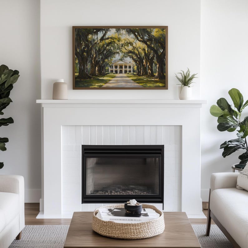 May include: A white fireplace with a black fireplace insert and a framed painting of a white mansion with a long driveway lined with trees. The painting is above the fireplace and there is a white vase on the mantle.