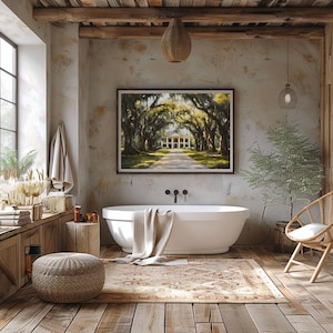 May include: A white freestanding bathtub with a beige towel draped over the edge, set in a rustic bathroom with exposed wooden beams, a large framed painting of a Southern plantation, and a woven rug on the floor.