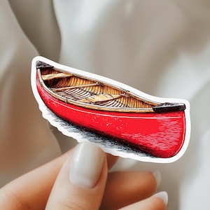 May include: A sticker featuring a detailed illustration of a bright red canoe with a tan wooden interior. The canoe has black end caps and visible cross-ribbing along the hull, rendered with fine black ink lines to show texture and depth.