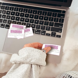 May include: Rectangular white stickers with pink text reading WARNING I get distracted by fancy saddles, pretty headstalls, fast, shiny horses, and sparkly things. The stickers are placed on the metallic surface of a laptop keyboard area.