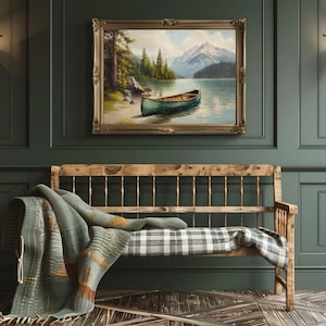 May include: A framed landscape painting depicts a teal canoe on a lake with mountains in the background. Below, a wooden bench with a plaid cushion is draped with a green and orange patterned blanket. The room has dark green walls and a wooden floor.