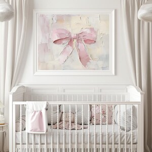 May include: A white crib with a pink and white blanket and pillows. A framed painting of a pink bow hangs above the crib.