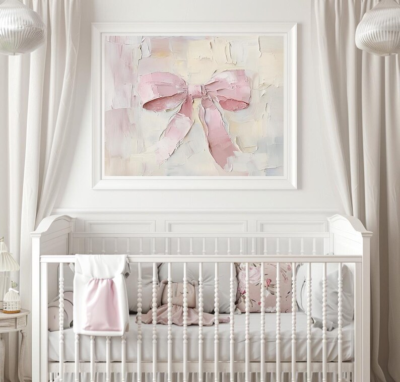May include: A white crib with a pink and white blanket and pillows. A framed painting of a pink bow hangs above the crib.