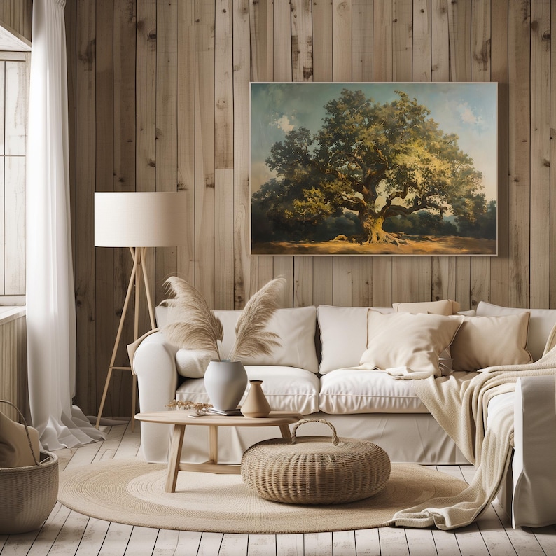May include: A living room interior with a white sofa, a wooden coffee table, and a large framed painting of a tree on a wood wall. The painting is in a rustic style and features a large tree with green leaves and a brown trunk. The room is decorated with a beige rug, a wicker basket, and a floor lamp.