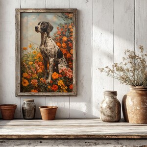 May include: A framed painting of a black and white dog sitting in a field of orange and yellow flowers. The painting is hanging on a white wood wall with a vase of dried flowers and three terracotta pots on a white wood shelf.