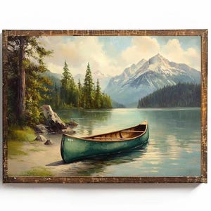 May include: A framed landscape painting depicts a serene lake scene with a green canoe resting on the shore. Towering mountains with snow-capped peaks are visible in the background, framed by lush green trees and a cloudy sky. The artwork is encased in a rustic brown wooden frame.
