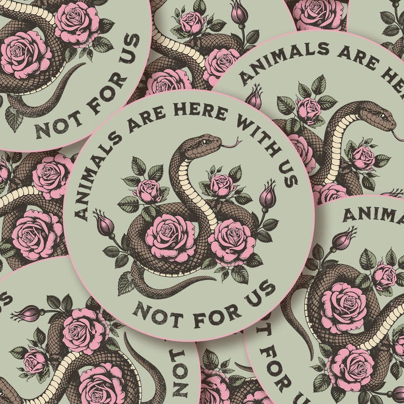 May include: Round sticker with a snake and pink roses design. The text "ANIMALS ARE HERE WITH US" and "NOT FOR US" is printed around the edge of the sticker. The snake is brown and the roses are pink.