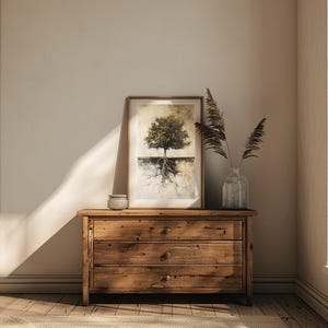 May include: A wooden dresser with three drawers, a framed print of a tree with roots, and a vase with dried flowers on top. The dresser is in a room with beige walls and wooden floors.