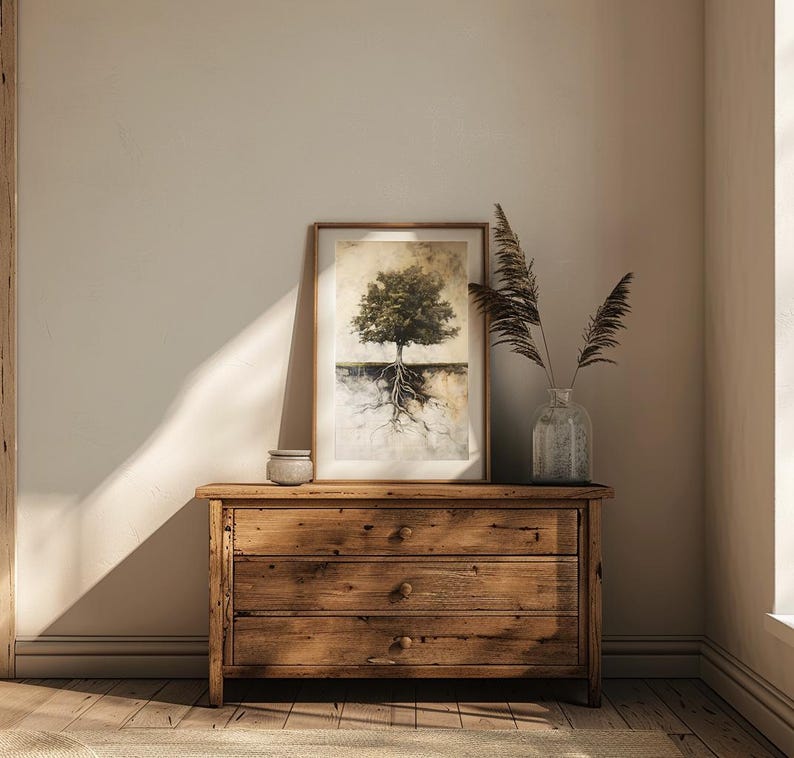 May include: A wooden dresser with three drawers, a framed print of a tree with roots, and a vase with dried flowers on top. The dresser is in a room with beige walls and wooden floors.