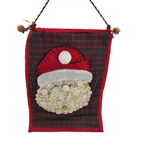May include: A red and green plaid fabric stocking with a white button-covered Santa face. The stocking has a loop at the top for hanging.