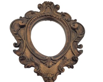 May include: A gold-toned ornate picture frame with a round opening. The frame has a detailed, intricate design with a distressed finish.