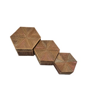 May include: Three hexagonal decorative boxes in varying sizes. The boxes are made of woven material in shades of brown and tan, with a starburst pattern on the lids. The boxes are arranged diagonally, showcasing their different sizes.