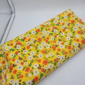 May include: Yellow fabric with a white and orange floral print. The fabric has a textured surface.