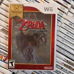 May include: A Nintendo Wii game case for "The Legend of Zelda: Twilight Princess." The game case has a red border and features artwork of a character with long hair and a wolf. The game is rated "T" for Teen.