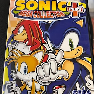 May include: A PlayStation 2 game case for Sonic Mega Collection Plus. The cover features Sonic the Hedgehog, Knuckles, and Tails. The game case has the ESRB rating and the SEGA logo.