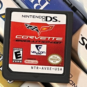 May include: A black Nintendo DS game cartridge featuring the game "Corvette Evolution GT." The cartridge has a red background with the Corvette logo and the ESRB rating "E" for Everyone. The text "NTR-AVXE-USA" is printed at the bottom.