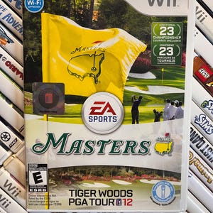 May include: A Wii game case for "Tiger Woods PGA Tour 12: Masters" featuring a yellow flag with the Masters logo. The case includes the EA Sports logo, the Wii logo, and the ESRB rating. The game includes 23 championship courses.