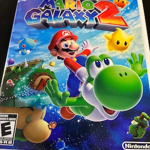 May include: Super Mario Galaxy 2 Wii game case. The cover features Mario riding Yoshi, with a vibrant blue galaxy background. The game title is prominently displayed with the Wii logo in the upper right corner. The ESRB rating is visible.