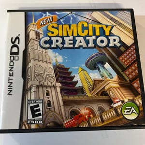 May include: A Nintendo DS game case for "SimCity Creator." The cover art features a cityscape with various architectural styles, including a pagoda and modern skyscrapers. The game case is black with the Nintendo DS logo on the side and the ESRB rating.