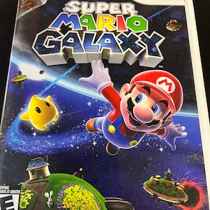 May include: Super Mario Galaxy Wii game case. The cover features Mario in a red cap and overalls, set against a starry galaxy backdrop. The game's title is prominently displayed. A yellow star-shaped character is also visible.