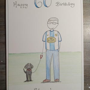 May include: Hand-drawn birthday card with the text "Happy 60th Birthday" in black and blue. The card features a cartoon illustration of a man in a jersey with a dog on a leash. The dog is black with a red collar. The name "Steve!" is written at the bottom.