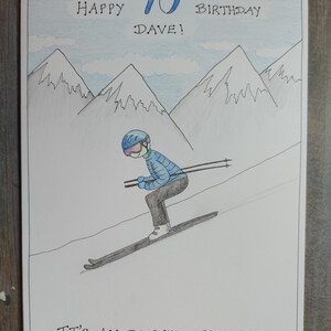 May include: Hand-drawn birthday card with a skier on a snowy slope, mountains in the background, and the text "Happy 70th Birthday Dave!" and "It's All Downhill From Here."