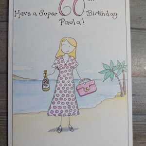 May include: Hand-drawn birthday card with the text "Have a Super 60th Birthday Paula!" A woman in a pink polka dot dress stands on a beach holding a purse and a champagne bottle. Palm trees and ocean in the background.