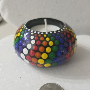 May include: A black candle holder with a rainbow polka dot design. The holder is round and has a small white candle inside.