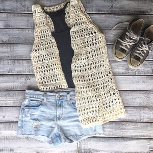 May include: A crocheted cream-colored vest with a black tank top underneath, blue denim shorts, and a pair of brown canvas sneakers.