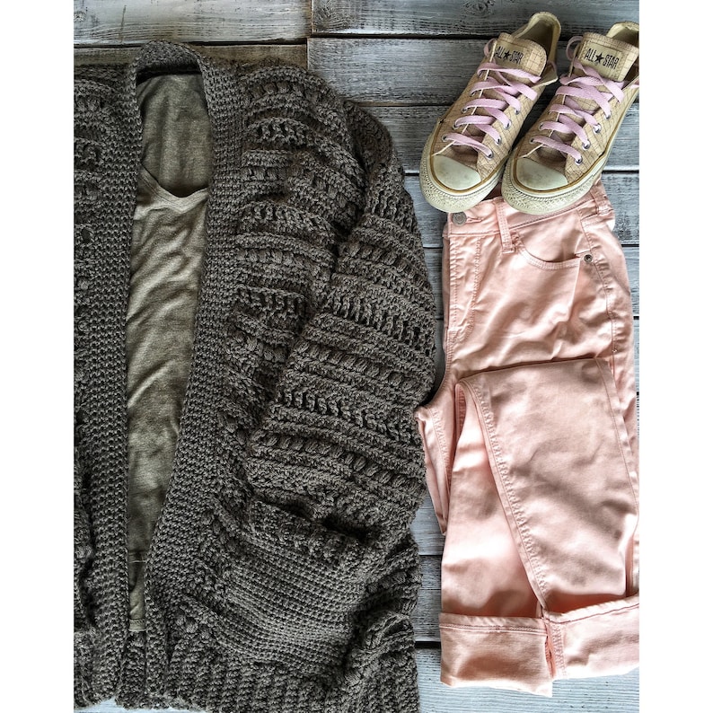 May include: A brown crocheted cardigan with a light brown t-shirt underneath. Pink jeans and a pair of tan canvas sneakers with pink laces are also pictured.