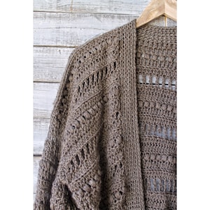 May include: A brown crocheted cardigan with a lacy openwork design. The cardigan has a long, open front and is hanging on a wooden hanger.