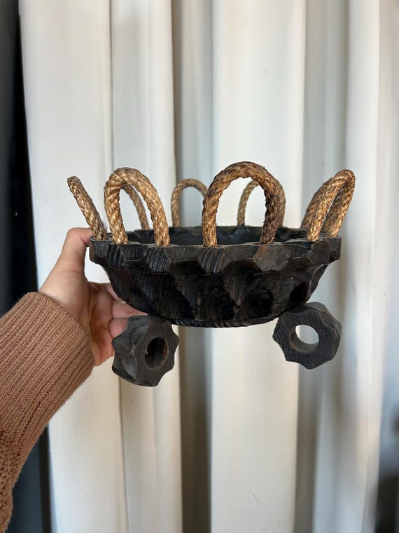 Hand-carved wooden bowl with rope handles that leans full brutalist-craft — the rope detail elevates it from plain bowl to actual decor object.