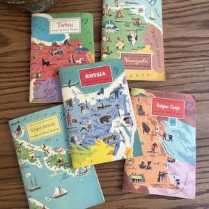May include: Five vintage American Geographical Society Around the World Program booklets featuring illustrated maps of Turkey, British Guiana, Venezuela, Russia, the Virgin Islands, and the Belgian Congo, each with colorful regional graphics and text.