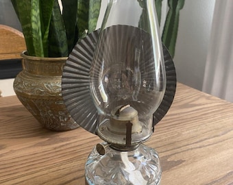 Könnte beinhalten: Transparente Glas-Öllampe mit Metallreflektor und dem Text "Yukon Jack" auf dem Sockel. Die Lampe hat ein dekoratives, geätztes Design und einen Docht. Die Lampe steht auf einer Holzoberfläche.