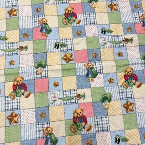 Puede incluir: Una tela de patchwork con un patrón repetido de osos de peluche, estrellas y otros elementos caprichosos. Los cuadrados son de colores pastel como rosa, azul, verde y amarillo, creando un diseño alegre. Ideal para mantas de bebé o manualidades infantiles.