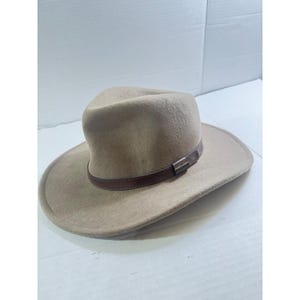 May include: A tan-colored fedora-style hat with a wide brim. The hat features a brown leather band around the crown with a silver-colored metal buckle. The hat is made of a soft, felt-like material.