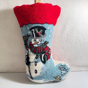 Puede incluir: Un calcetín navideño con un diseño de muñeco de nieve. El calcetín tiene un puño rojo y un cuerpo azul claro con un muñeco de nieve que lleva un sombrero de copa y una bufanda. El muñeco de nieve sostiene una escoba. El calcetín mide aproximadamente 46 cm de largo.