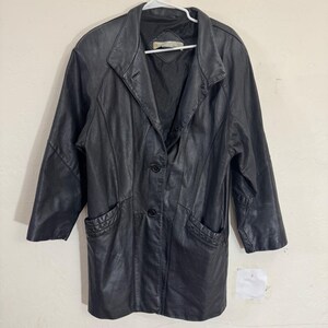 May include: Black leather jacket with a notched collar, three-quarter sleeves, and two front pockets. The jacket has a button-down closure and is hanging on a white hanger. The leather appears to be slightly worn.
