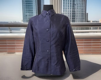 May include: A navy blue button-down shirt with long sleeves. The shirt has a classic collar and is displayed on a black mannequin. The fabric has a subtle sheen. The background features a cityscape with tall buildings.