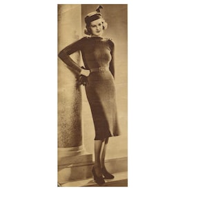 May include: A vintage sepia photograph of a woman in a long-sleeved, figure-hugging dress and matching hat. The dress has a belt at the waist and button details on the shoulders. She wears gloves and heels, posing near a column.