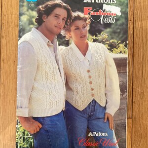 Puede incluir: Portada de un libro de patrones Patons Fashion Vests vintage. La portada presenta a un hombre y una mujer con chalecos de punto de cable color crema sobre camisas y vaqueros azules. El texto incluye "Fashion Vests" y "Classic Wool".