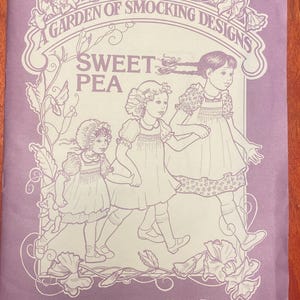 May include: A lavender-colored sewing pattern cover with the text "A GARDEN OF SMOCKING DESIGNS" and "SWEET PEA." The cover features line drawings of three girls in dresses. The text "Pinafore and Basic Yoke Dress" is at the bottom.